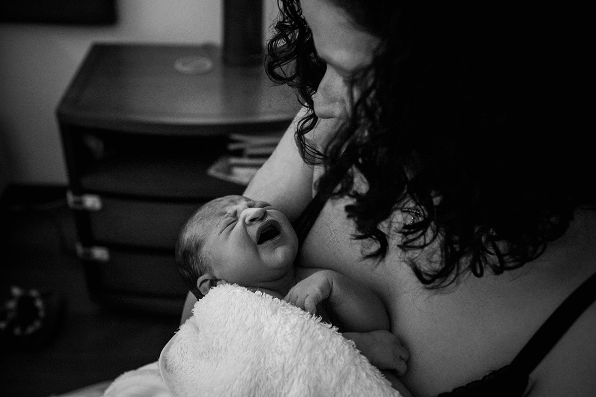 mãe observa seu bebê nos braços  após o nascimento em foto de Adriana Costa