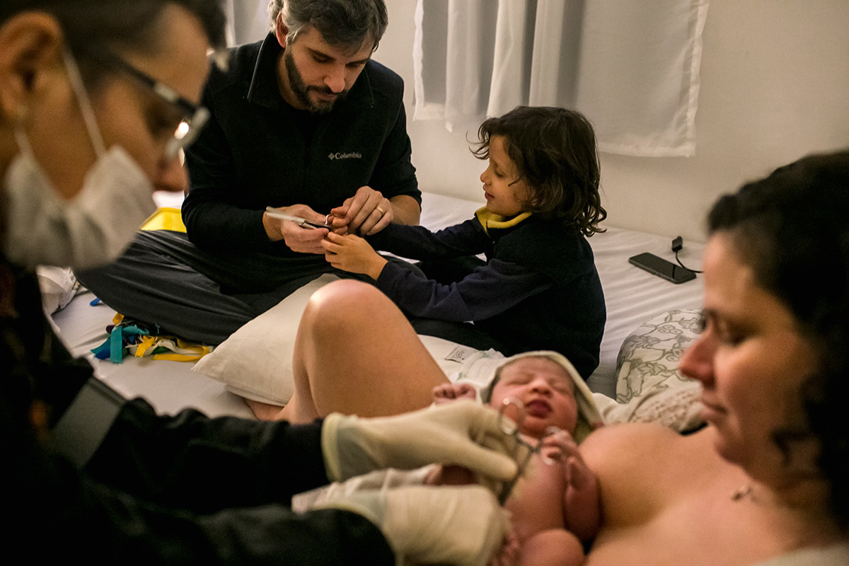 bebê sendo preparado para o corte do cordão umbilical que será feito por seu pai e seu irmão mais velho, em foto de Adriana Costa