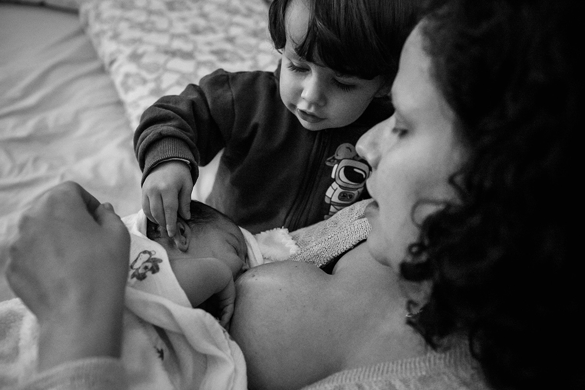 menino pega curioso na orelha do seu irmão recém-nascido enquanto ele ammaenta