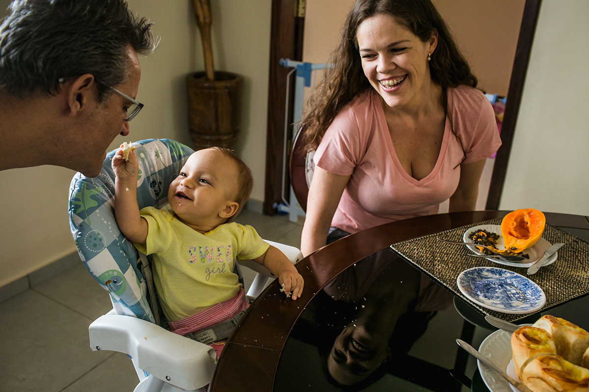 bebê oferece sorrindo um pedaço de pão para o seu pai, em foto de Adriana Costa