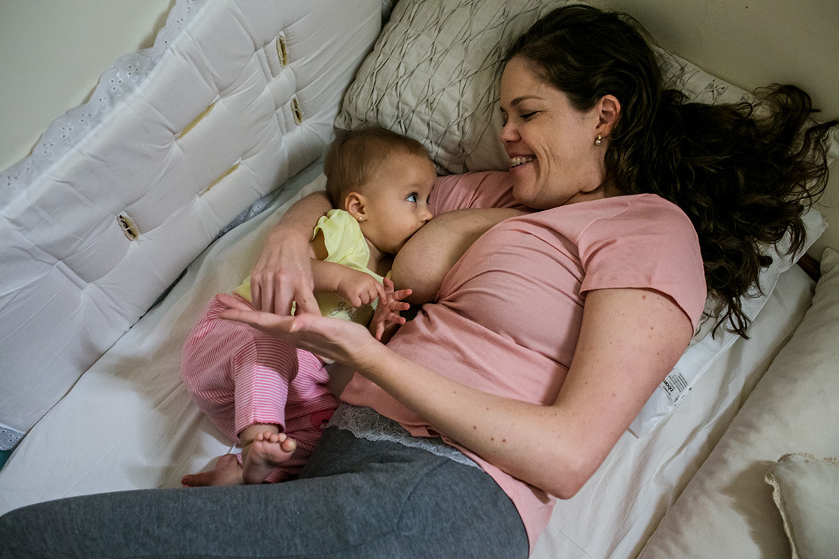 Foto de Adriana Costa da mãe amamentando e cantando pintinho amarelinho para sua bebê
