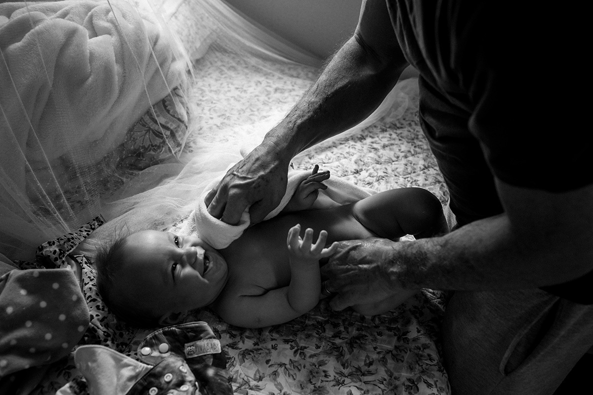 bebê sorri enquanto seu pai enxuga com a toalha seu pescoço