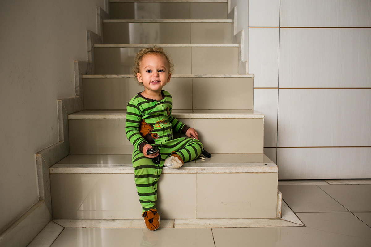 menino de um ano assenta feliz na escada de sua casa com o nariz escorrendo, por adrianacostafotos