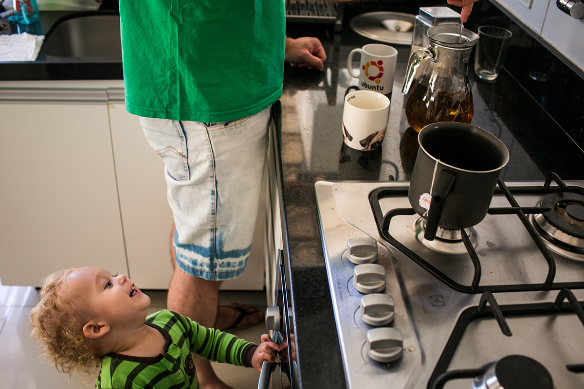 foto de Adriana Costa do menino de um ano observando feliz seu pai preparar o chá no fogão 
