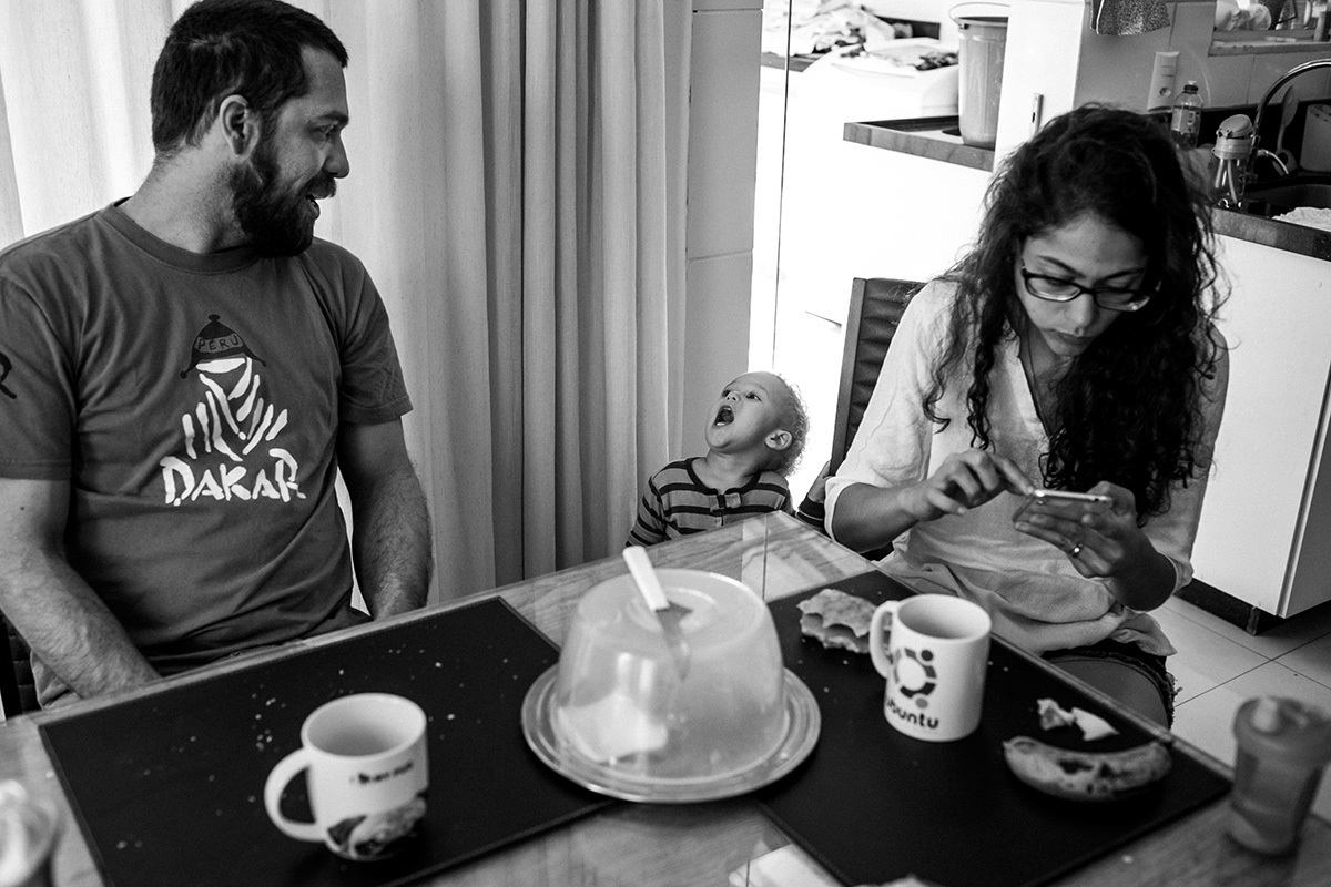 criança brinca com seu pai enquanto ele toma o café da manhã, em foto de Adriana Costa