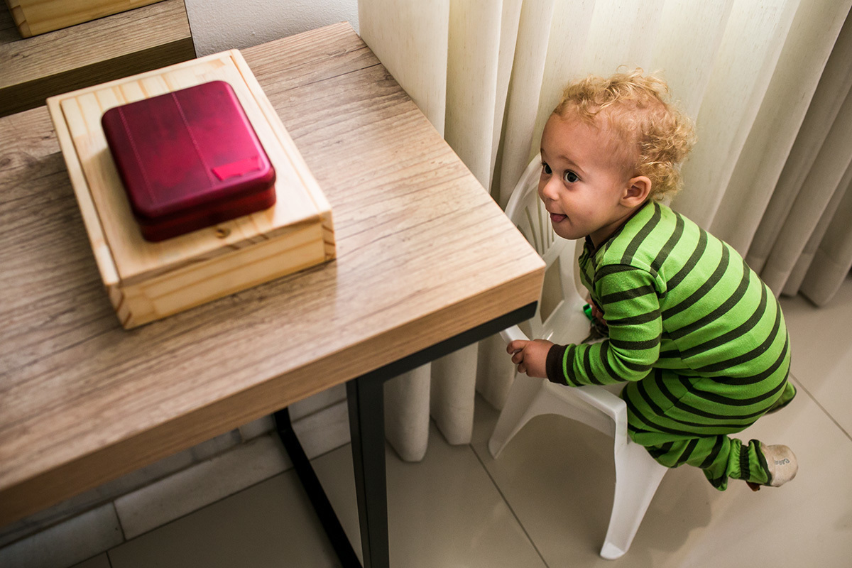 menino de um ano subindo na cadeira para alcançar um objeto, por Adriana Costa