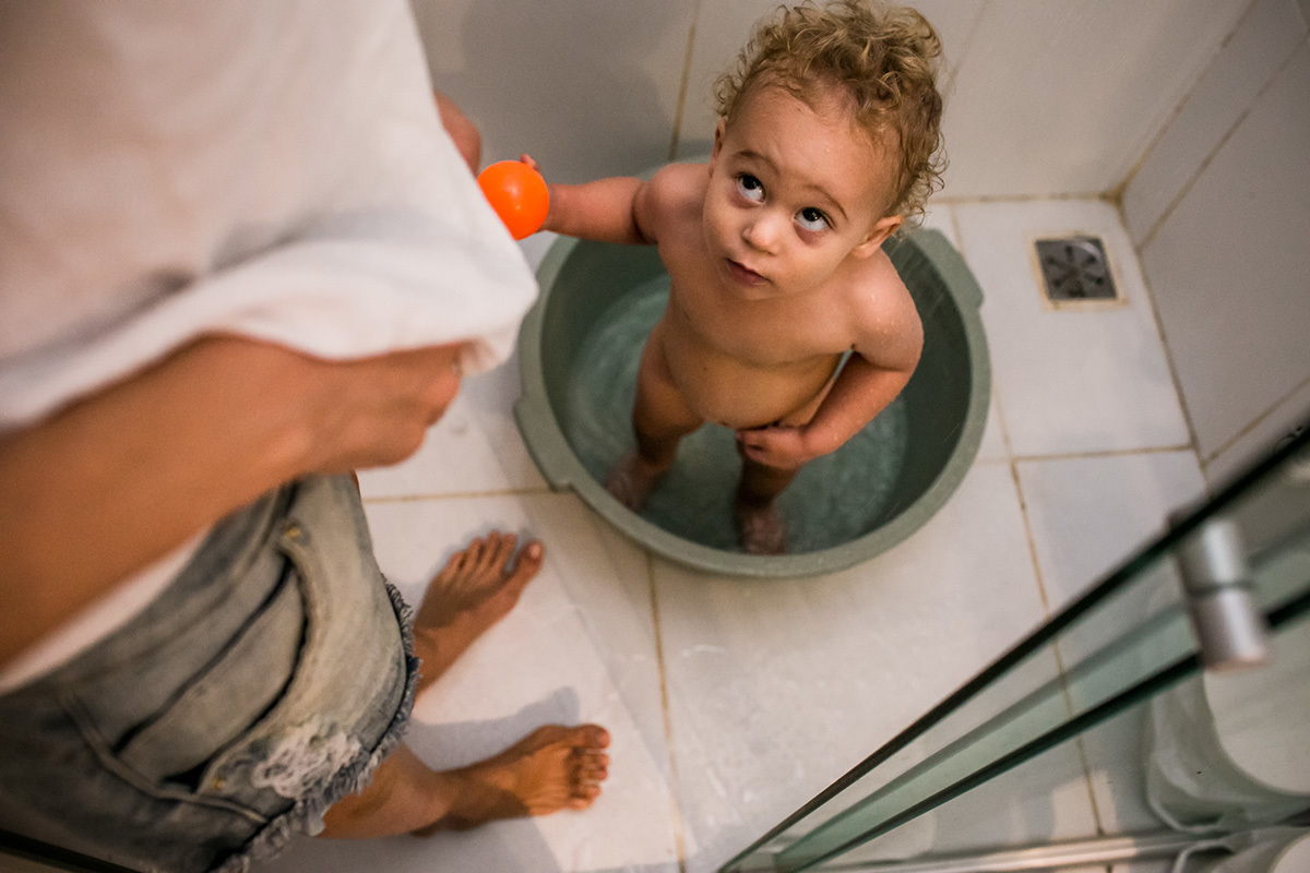 mãe e filho se preparam para tomar banho juntos durante um acompanhamento documental da família realizado por Adriana Costa