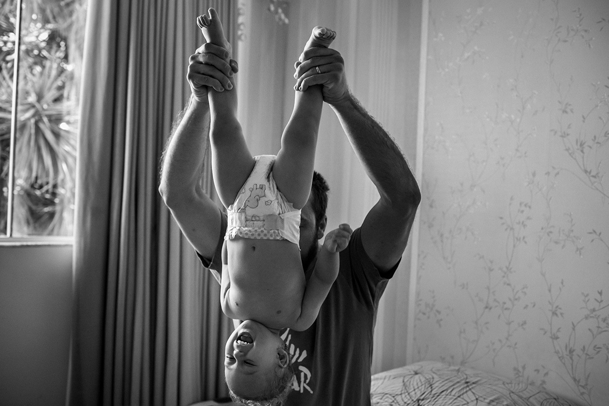 pai brinca de levantar seu filho de cabeça para baixo, por Adriana Costa