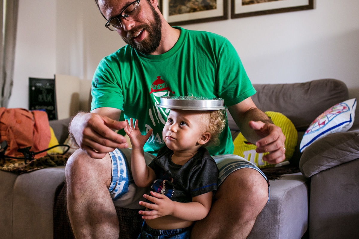 pai e filho brincam com um utensílio da cozinha como se fosse um chapéu, em foto de Adriana Costa
