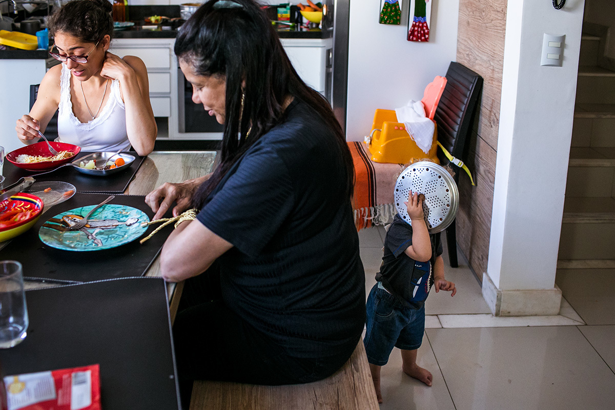 menino usa uma panela como celular enquanto sua mãe e avó almoçam