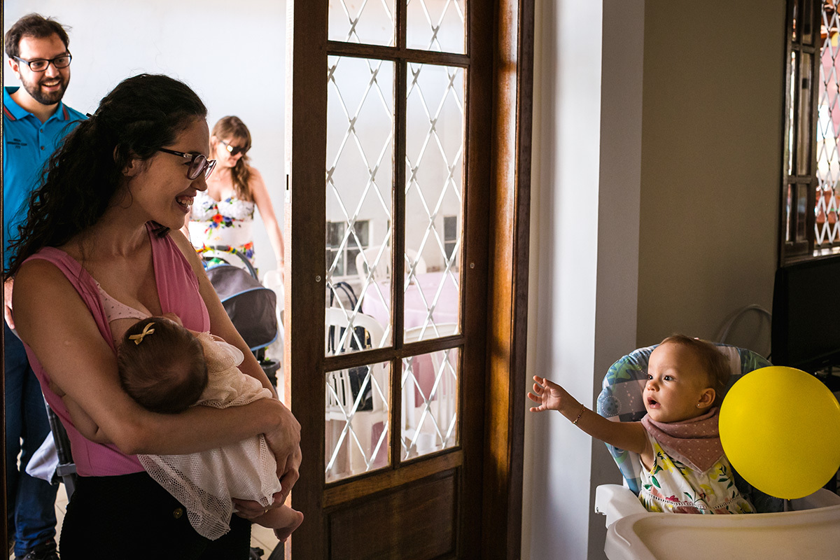 aniversariante recebendo seus convidados da sua cadeirinha de refeição, segurando seu balão, por Adriana Costa
