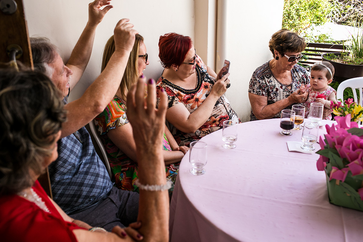 adultos brincando com um bebê para fazê-la rir durante uma festa infantil, em foto de Adriana Costa