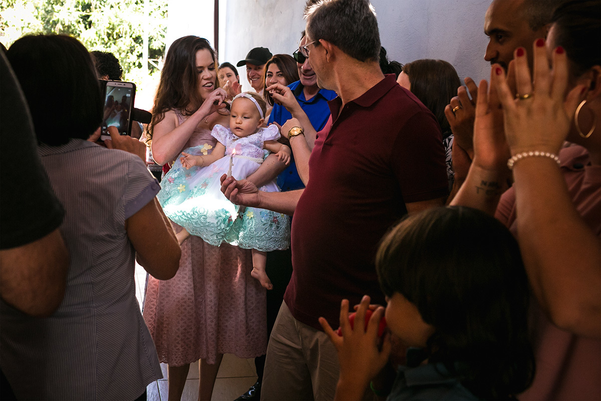 pais passando com sua bebê de 1 ano entre os convidados para cantar parabéns, em foto de Adriana Costa