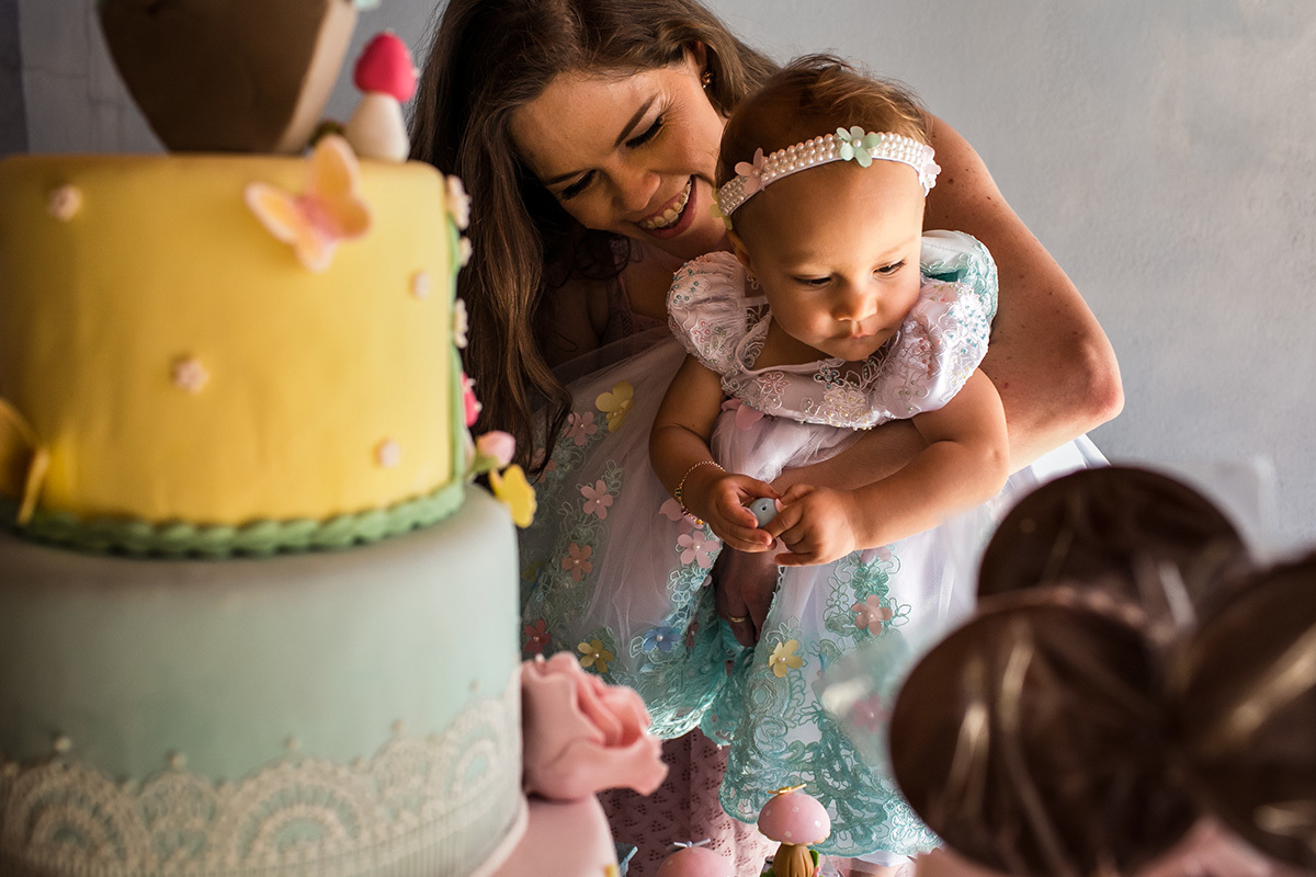 mãe mostrando para sua filha de 1 ano os doces e bolos da sua festa