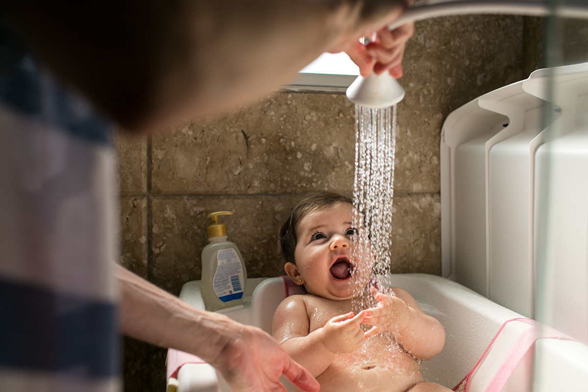 bebê se divertindo com a água do chuveirinho no banho, em foto de Adriana Costa