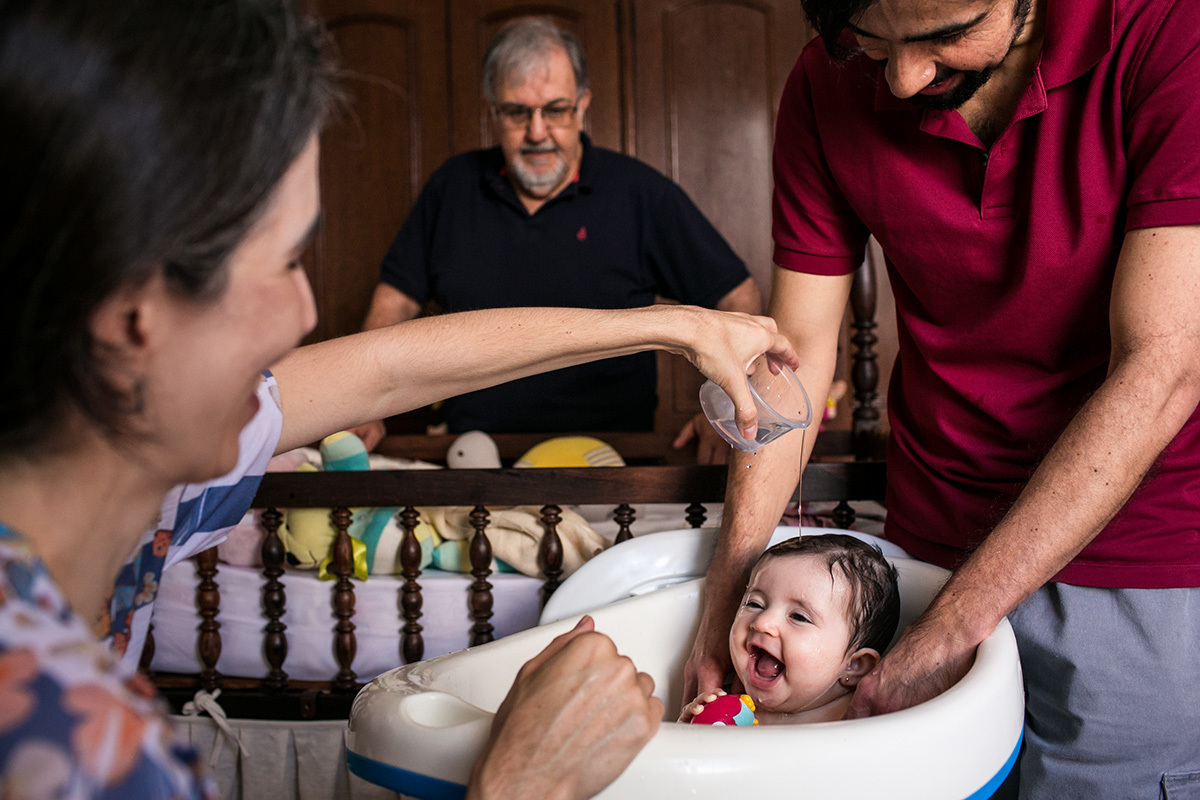 família reunida em volta do bebê que dá gargalhada no ofurô de bebê, por Adriana Costa