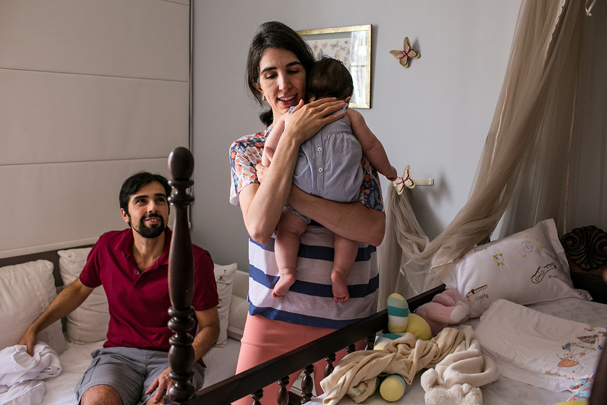 pai observa com carinho a sua filha sendo ninada pela mãe