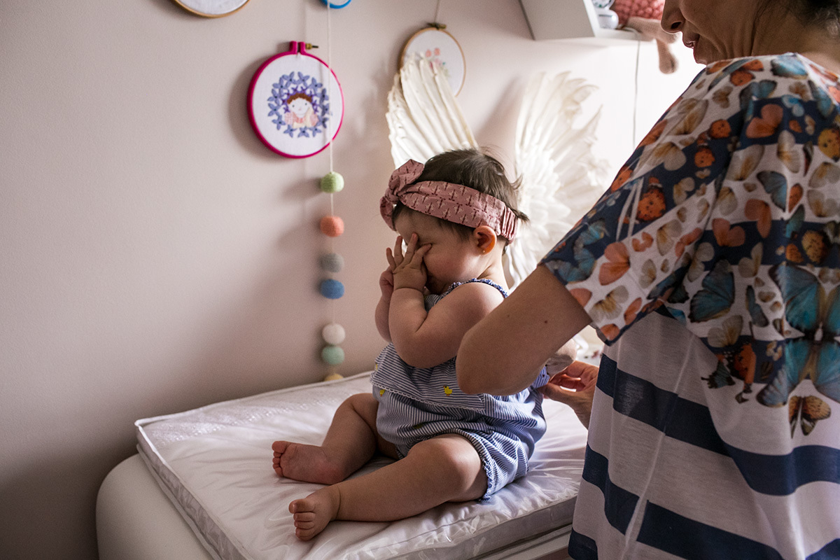 bebê coçando os olhinhos de sono enquanto sua mãe troca sua roupa