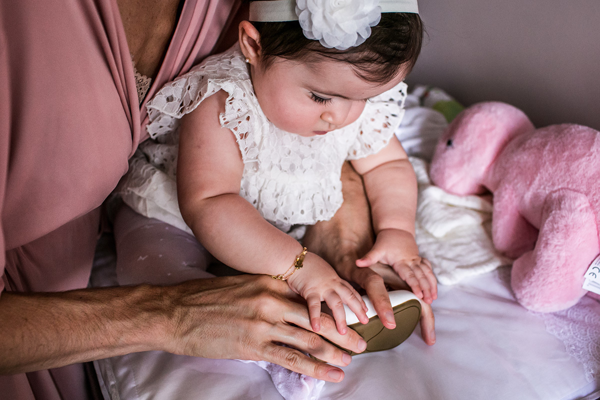 mãe vestindo o sapato na filha no dia da cerimônia de batismo