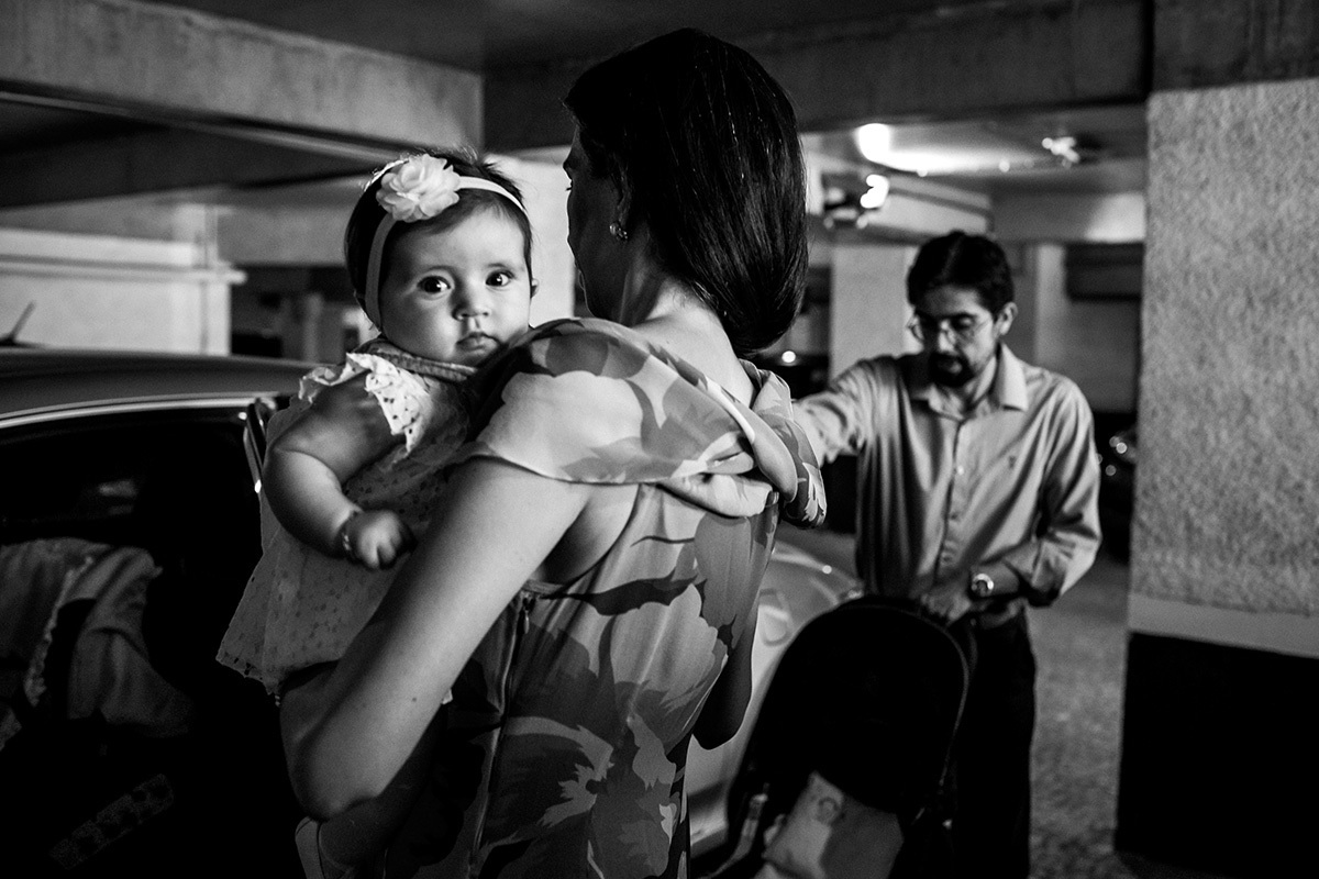 pais colocando a filha no carro para irem a sua cerimônia de batismo