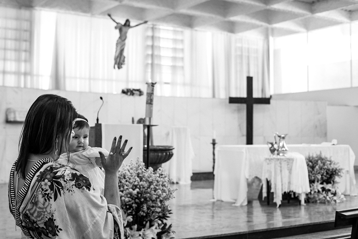 madrinha brincando com a afilhada durante a celebração de seu batizado na igreja, em foto de Adriana Costa