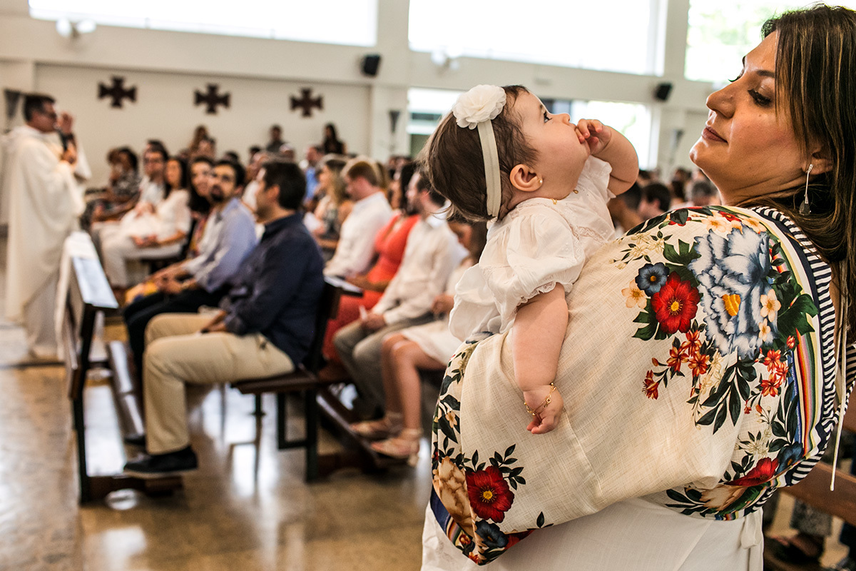 madrinha distrai a afilhada enquanto os pais prestam a atenção na missa de seu batizado