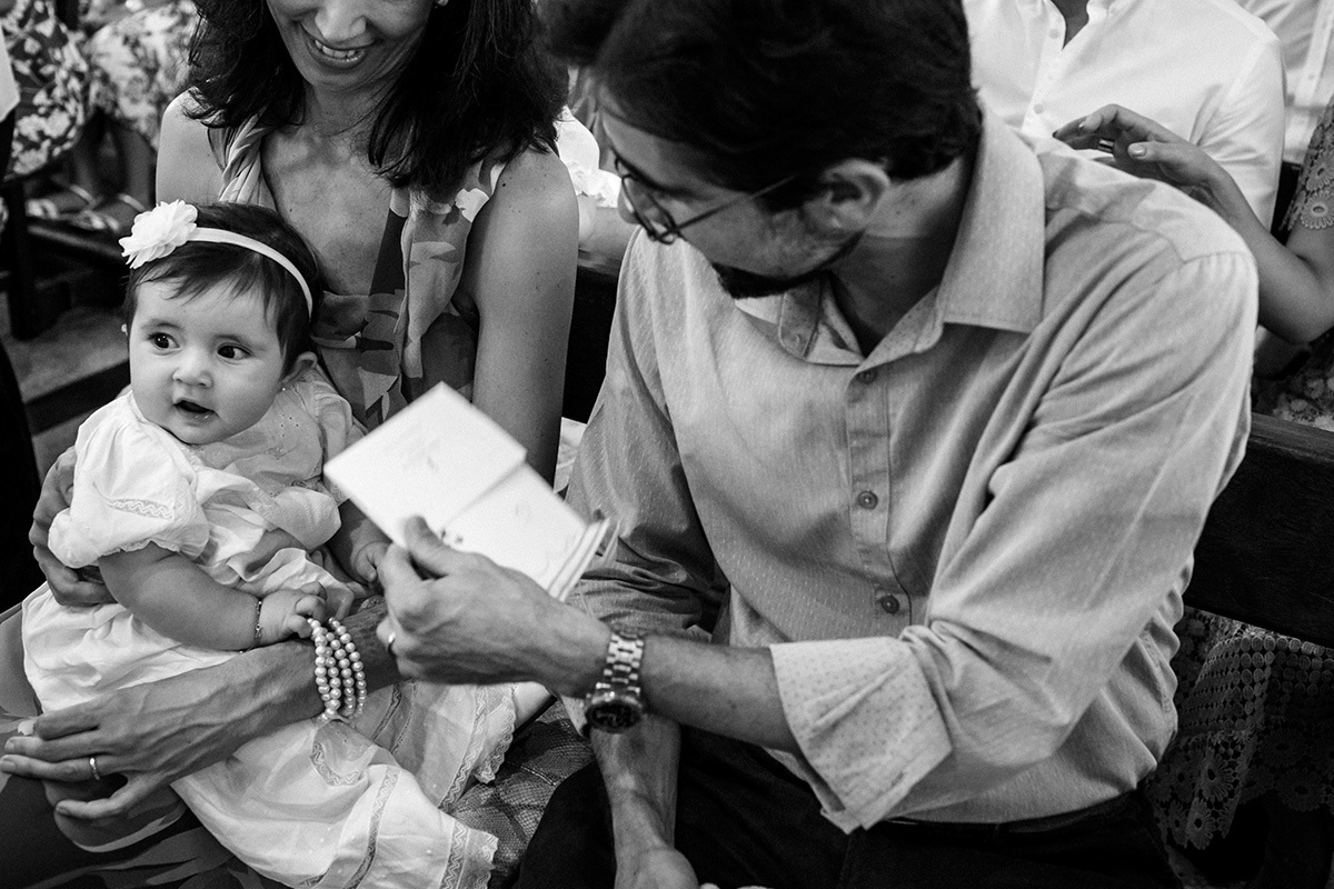 pais brincando com a filha durante sua cerimônia de batismo, em foto de Adriana Costa