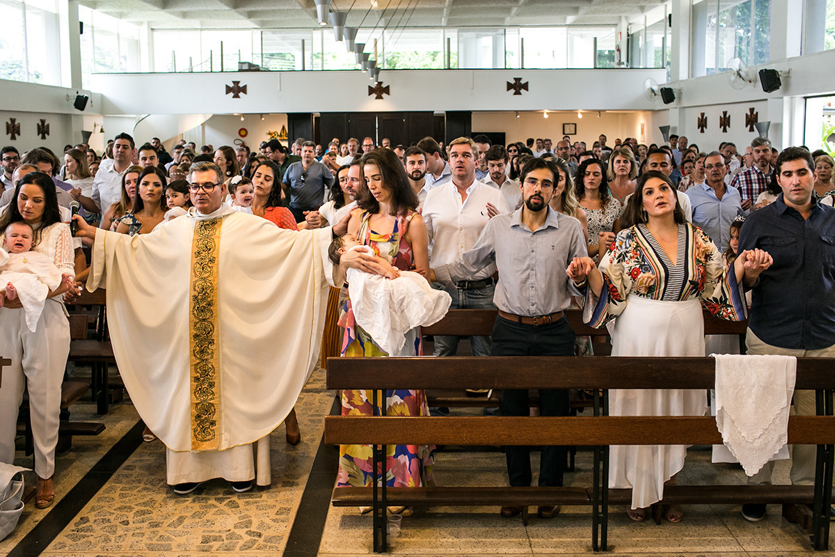 padre reza uma oração com todos de mãos dadas durante a cerimônia de batismo, por Adriana Costa