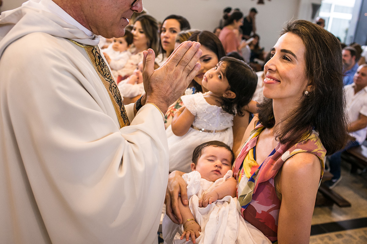 padre abençoa as mãe e seus bebês durante a cerimônia de batismo, em foto de Adriana Costa
