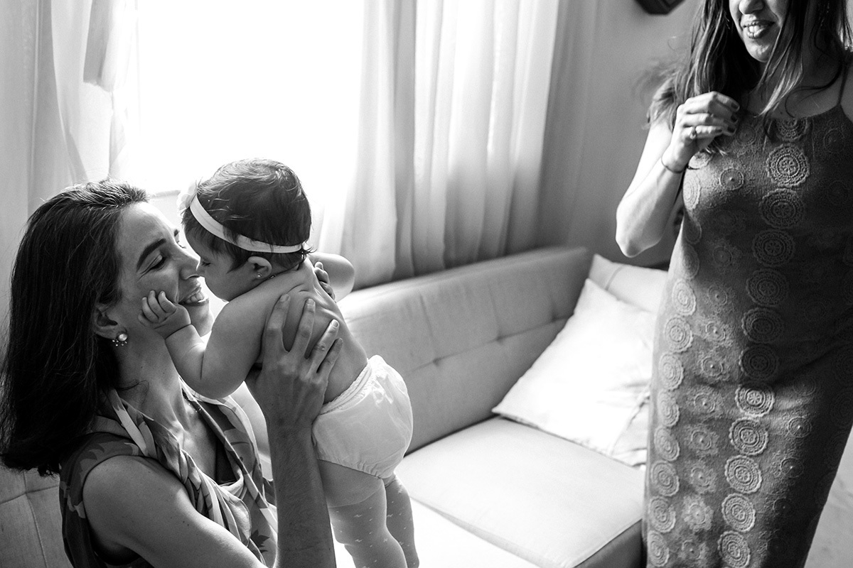 mãe pegando a filha com carinho para amamentá-la após o batizado, em foto de Adriana Costa