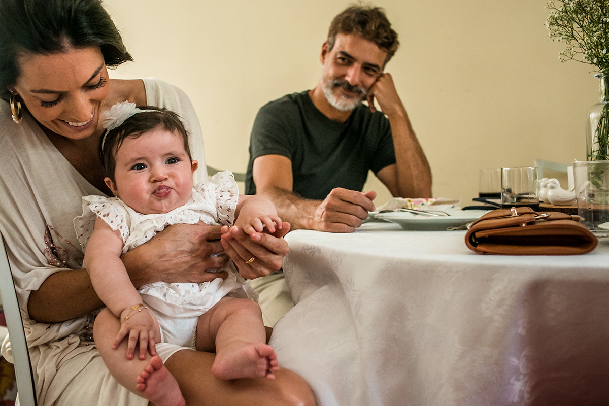 bebê fazendo careta no colo de uma de suas convidadas para sua festa de batismo, por Adriana Costa