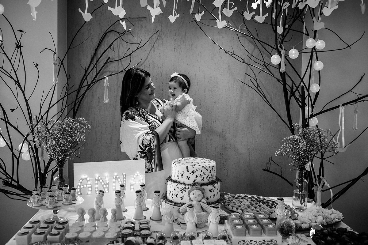 Foto de Adriana Costa da afilhada e madrinha próximo a linda mesa preparada para comemorar o seu batizado