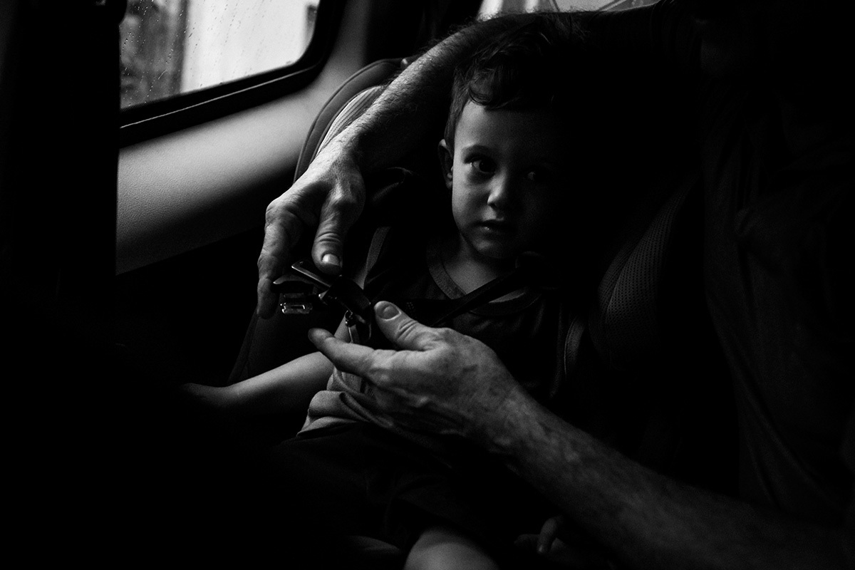 pai colocando o filho na cadeirinha do carro após a escola, por Adriana Costa