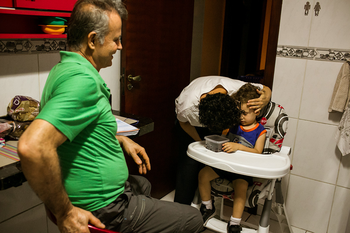 mãe dá um beijo no filho que está jantando com o pai ao chegar do trabalho