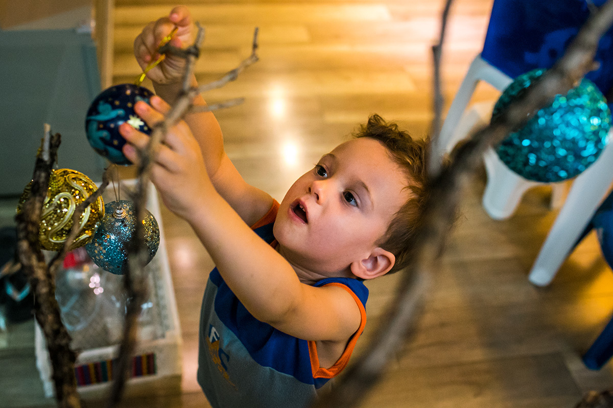 Foto de Adriana Costa do menino enfeitando a árvore de Natal da sua casa pela primeira vez