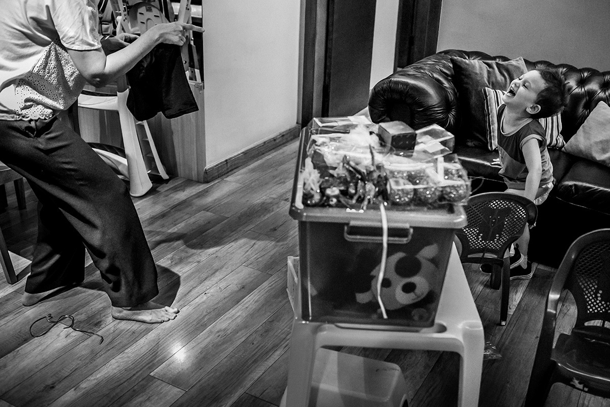 mãe corre atrás de seu filho, que está dando gargalhadas, para poder vestir sua calça após trocar sua fralda, em foto de Adriana Costa