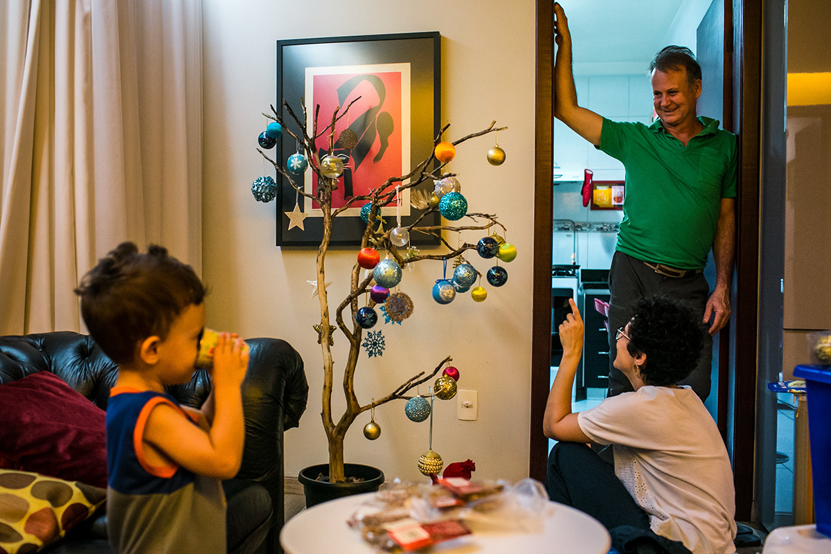menino bebe água, enquanto sua mãe e seu pai observam a árvore de Natal