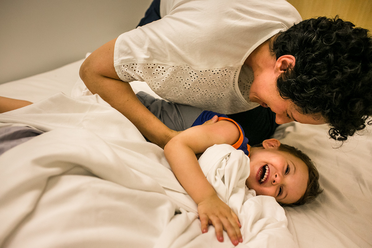 mãe e filho fazem brincadeiras na cama de casal, por Adriana Costa