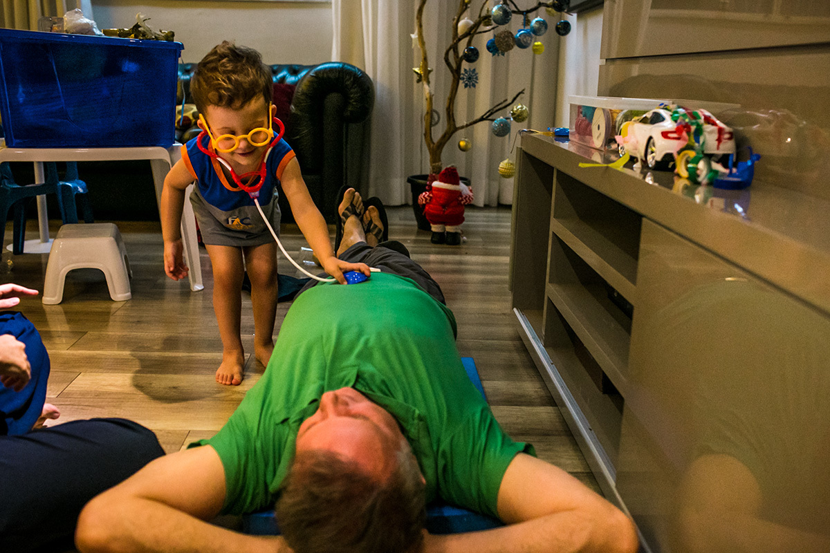 menino fantasiado de médico brinca de examinar o seu pai, em foto de Adriana Costa