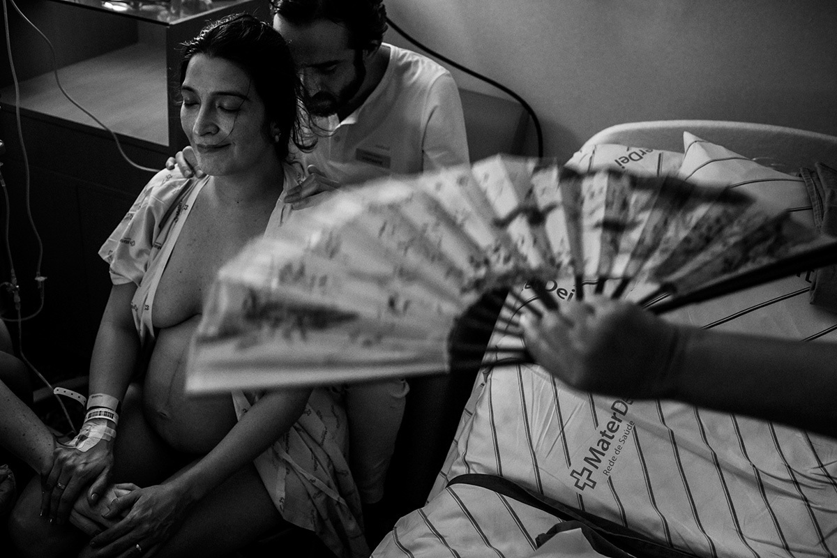 enfermeira obstétrica ventila com um leque casal grávido em trabalho de pato, em foto de Adriana Costa