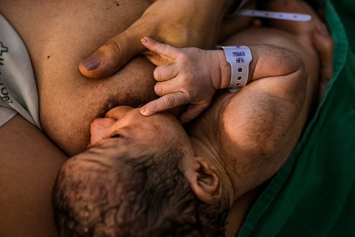 bebê amamenta logo após o nascimento com a mãozinha em um gesto de 