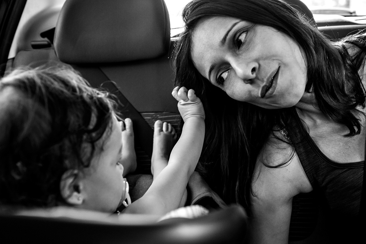 filha faz carinho no cabelo da mãe durante o trajeto de carro, por Adriana Costa
