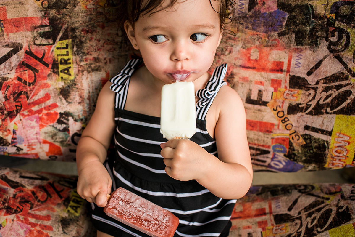 menina se delicia com dois picolés, em foto feita por Adriana Costa