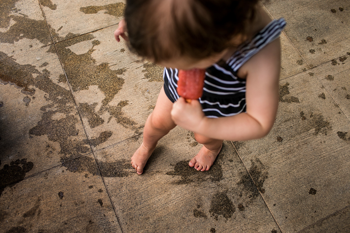 menina limpa o chão com o pezinho cheio de picolé que derreteu, em foto de Adriana Costa