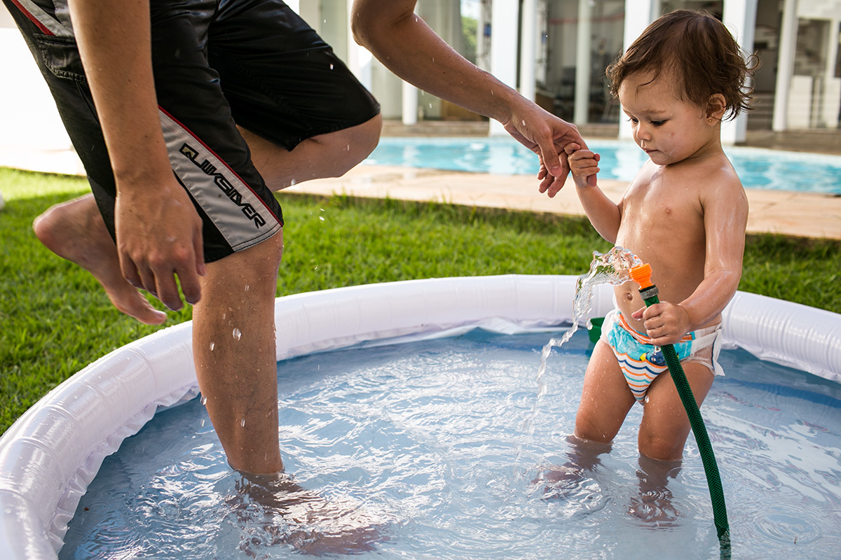 menina de 1 ano puxa seu pai para dentro da piscina inflável