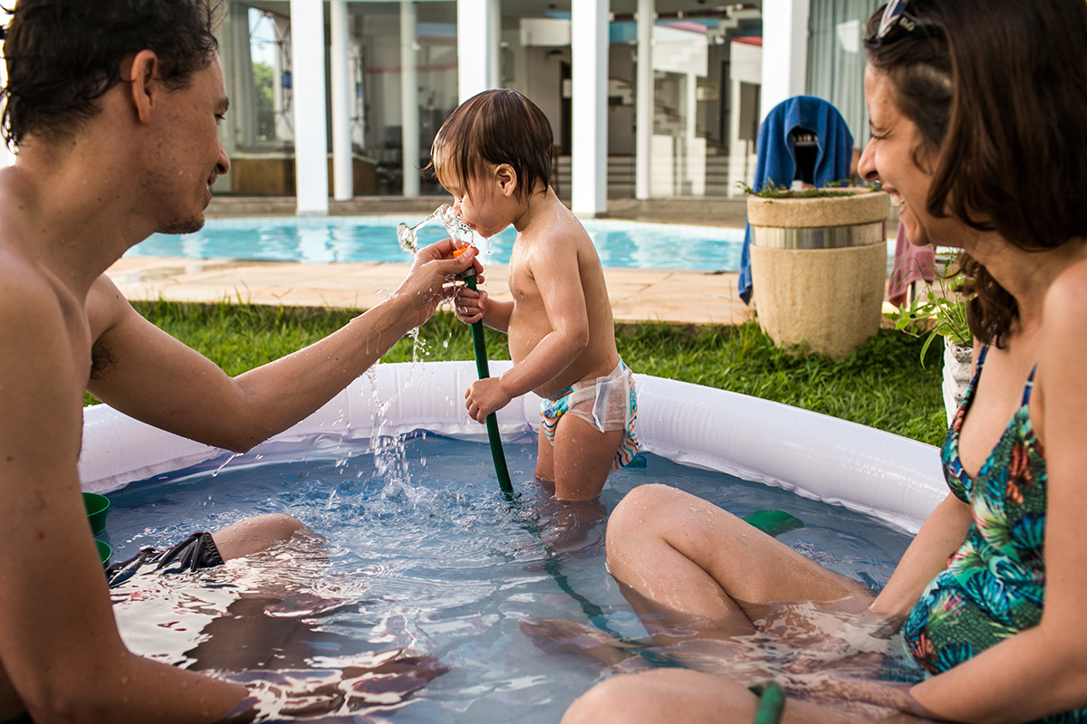 pais brincam com a filha na piscina e com a mangueira de água