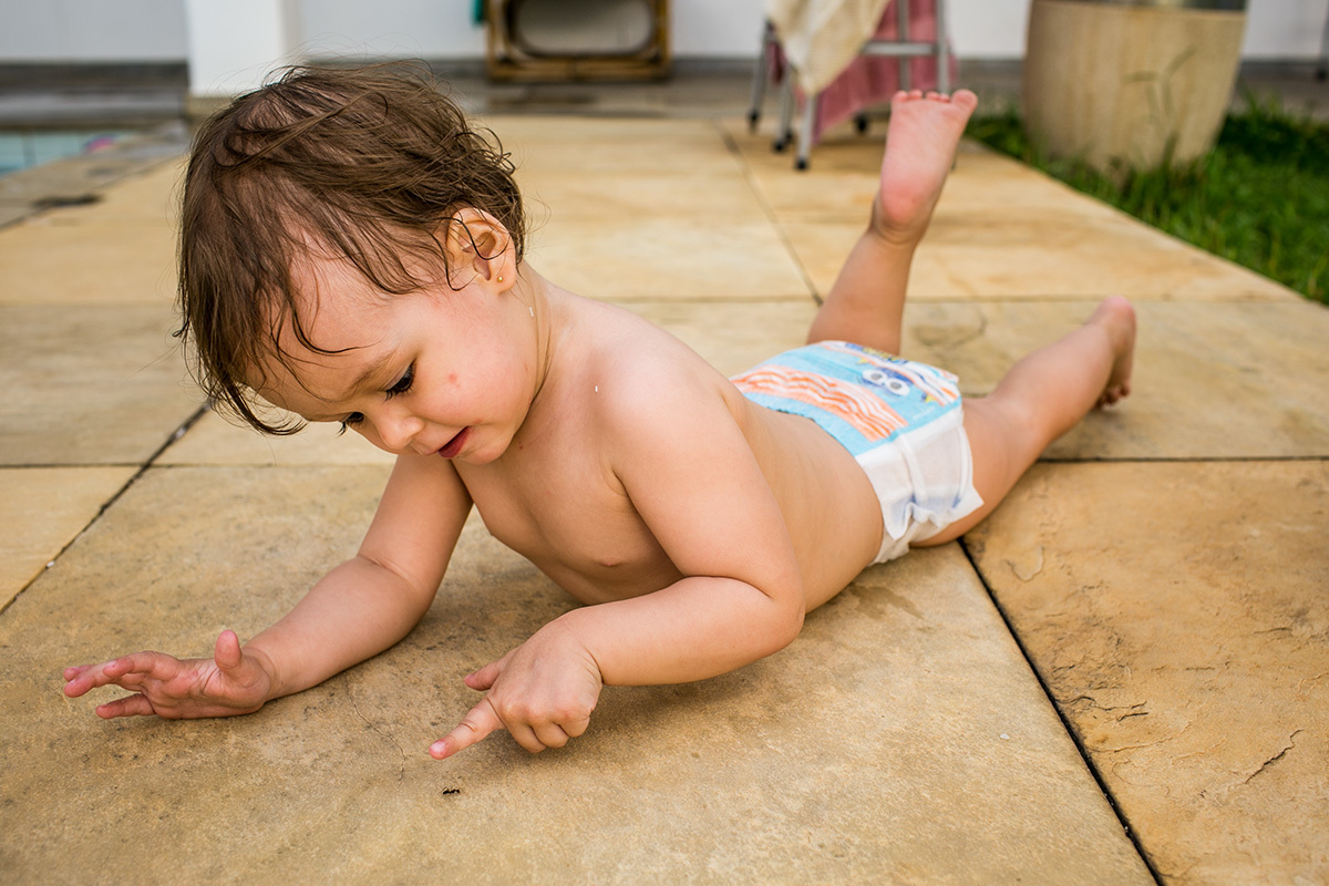 menina de um ano se diverte observando uma formiga, por Adriana Costa