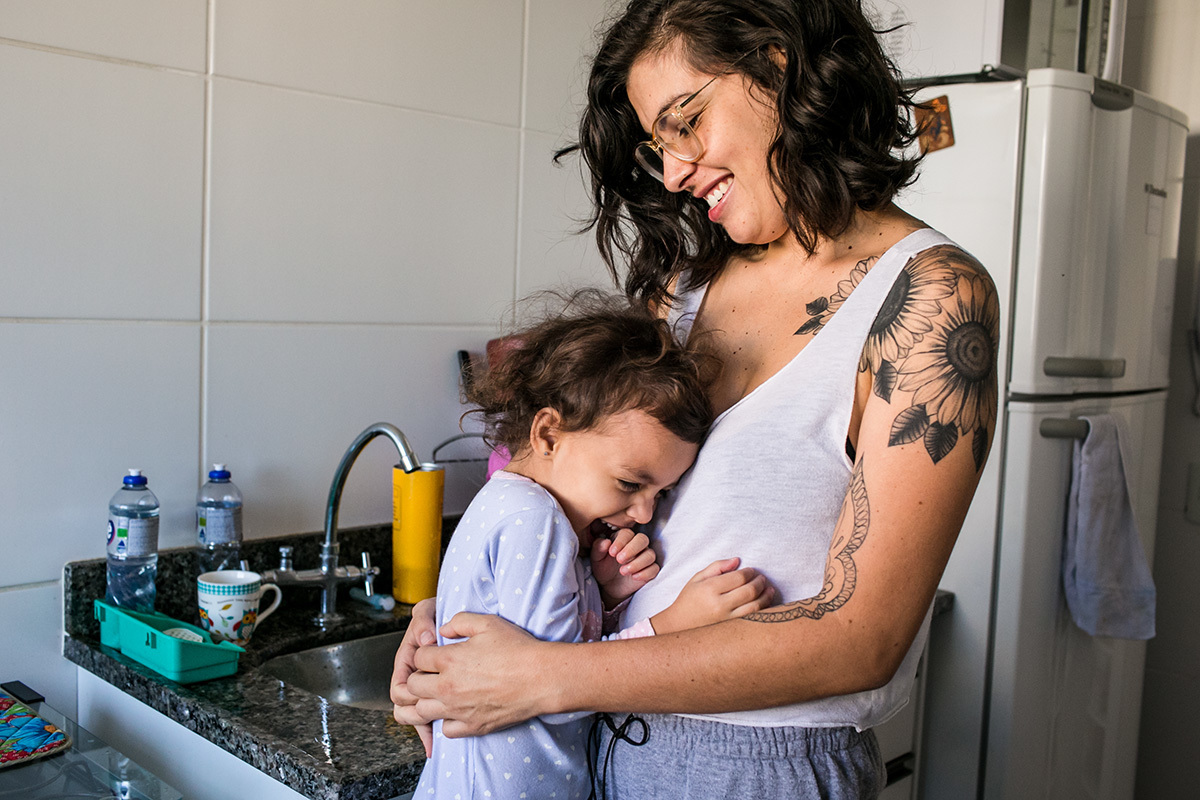 mãe fazendo cocegas na filha após terminar de lavar a louça, em foto de Adriana Costa