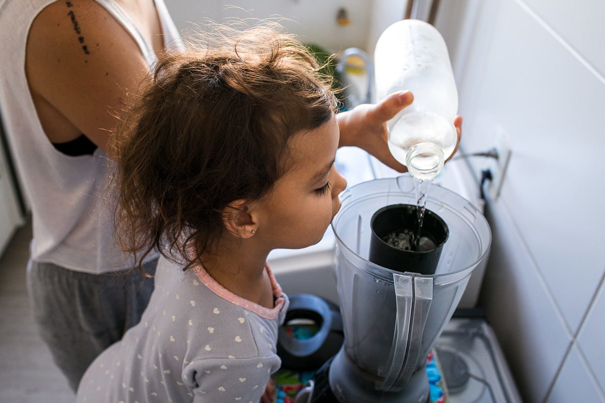 menina observa a mãe colocar a água no liquidificador para preparar a vitamina do café da manhã