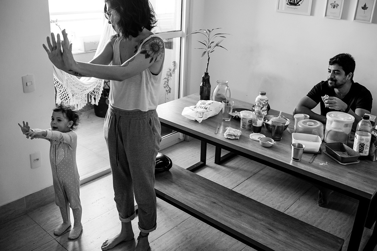pai observa sua esposa e filha brincarem enquanto toma o café da manhã